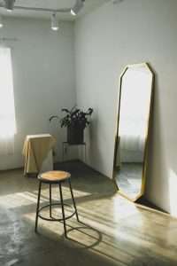 round brown wooden stool near a freestanding mirror