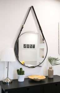 a round mirror is hanging with a black strap