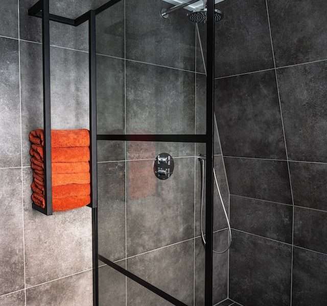 a bathroom with black tiles and stainless steel framed shower stall